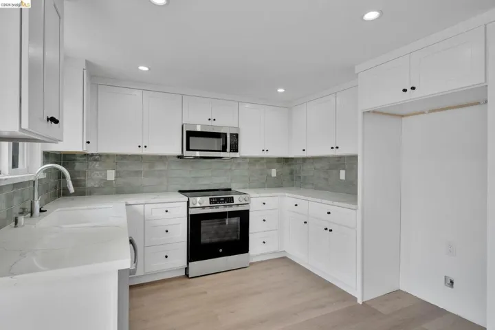 White shaker-style cabinetry with black hardware, stainless steel appliances, light-colored quartz countertops, and a textured green subway tile backsplash