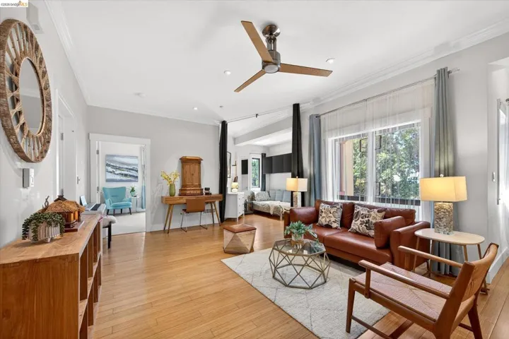 Spacious interior featuring wood-finish flooring, crown molding, a ceiling fan, large window with sheer and blackout curtains, and recessed lighting