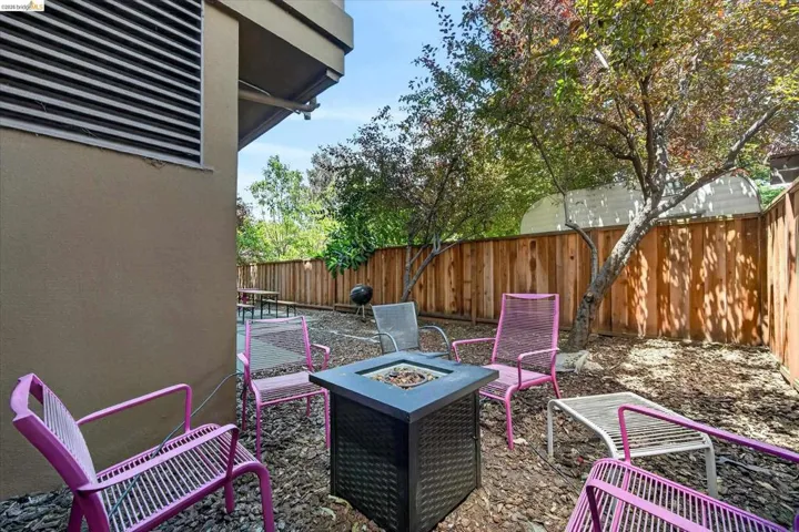 Private outdoor patio area featuring a built-in fire pit, privacy fencing, and mature trees