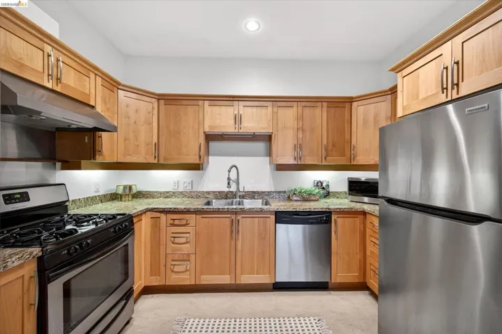 U-shaped kitchen featuring wood cabinetry, granite-finish countertops, stainless steel appliances, and a double basin sink with a high-arch faucet