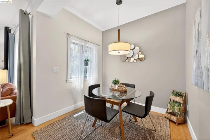 Dining area featuring warm wood-finish flooring, a contemporary pendant light fixture, and crown molding