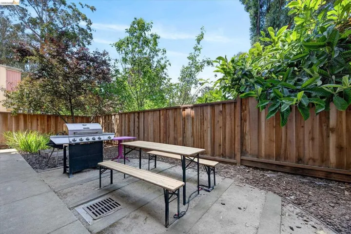 Paved patio area featuring a wooden privacy fence, mature perimeter trees, and landscaping elements