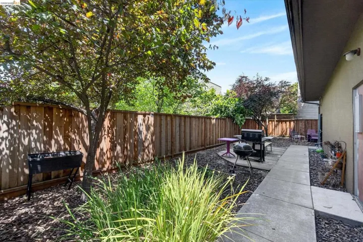 Private backyard featuring a concrete walkway, wood privacy fence, and mature trees