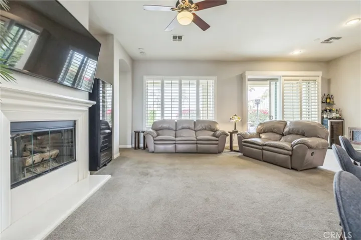The living room has a ceiling fan and a sliding glass door to the patio overlooking a large patio.


