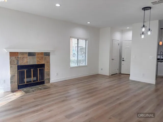 Spacious room featuring wood-finish flooring, a fireplace with a stone tile surround, and a single window with blinds