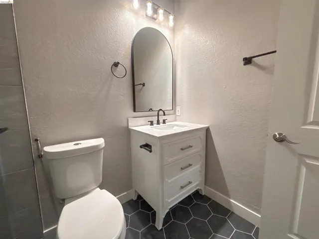 Bathroom featuring a white vanity with an integrated sink, dark hexagon tile flooring, and an arched mirror with overhead lighting