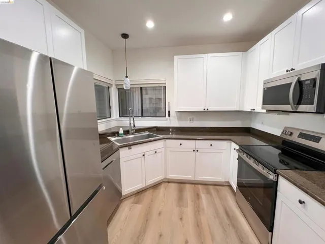 Modern kitchen featuring white shaker cabinetry, dark countertops, stainless steel appliances, and light wood-finish flooring