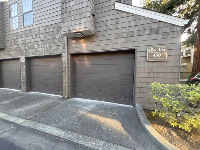 Shingle-sided exterior featuring three individual garage doors, concrete driveways, and a built-in outdoor light fixture