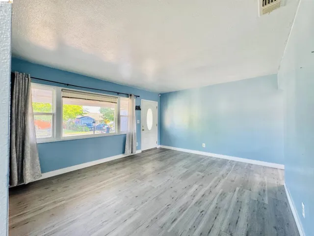 Spacious room featuring wood-finish flooring, a white entry door with an oval glass insert, and a large window
