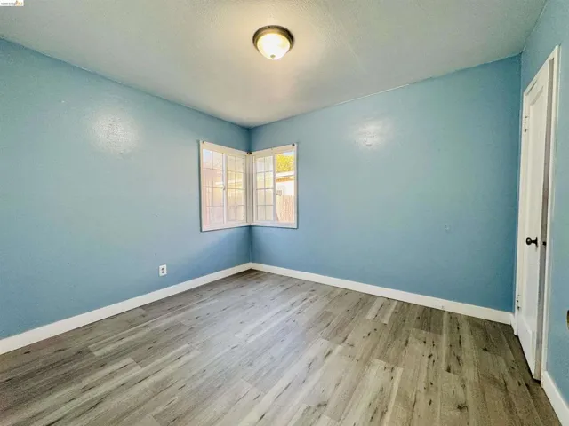 Room featuring wood-finish flooring, light blue walls, and white baseboards