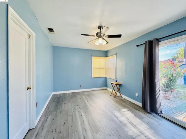 Room featuring light blue walls, wood-finish flooring, a ceiling fan with integrated lighting, and a sliding glass door providing exterior access