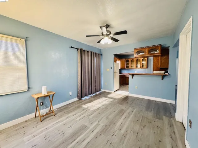 Open-concept living space featuring wood-finish flooring, a ceiling fan with integrated lighting, and a pass-through counter with overhead cabinetry