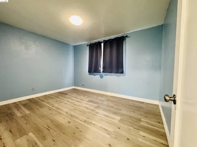 Room featuring wood-finish flooring, light blue walls, white baseboards, and a flush-mount ceiling light fixture