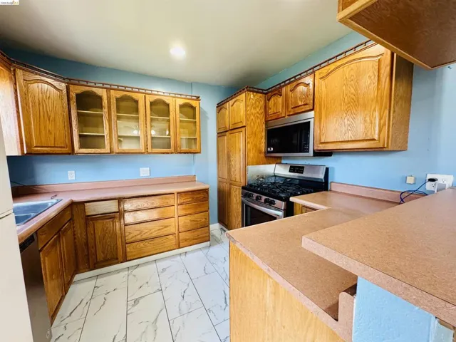 Kitchen featuring a gas range, over-the-range microwave, wood-finish cabinetry with some glass-front doors, and a double-tier counter space