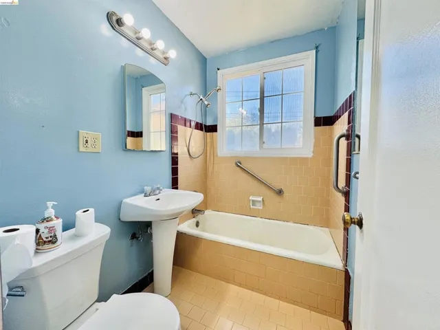 Bathroom featuring a pedestal sink, white bathtub, and tiled shower surround with a grab bar