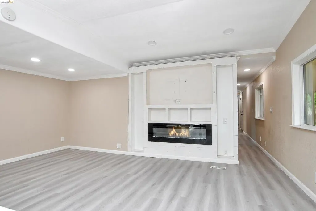 Unfurnished living room with ornamental molding, recessed lighting, light wood finished floors, and a glass covered fireplace