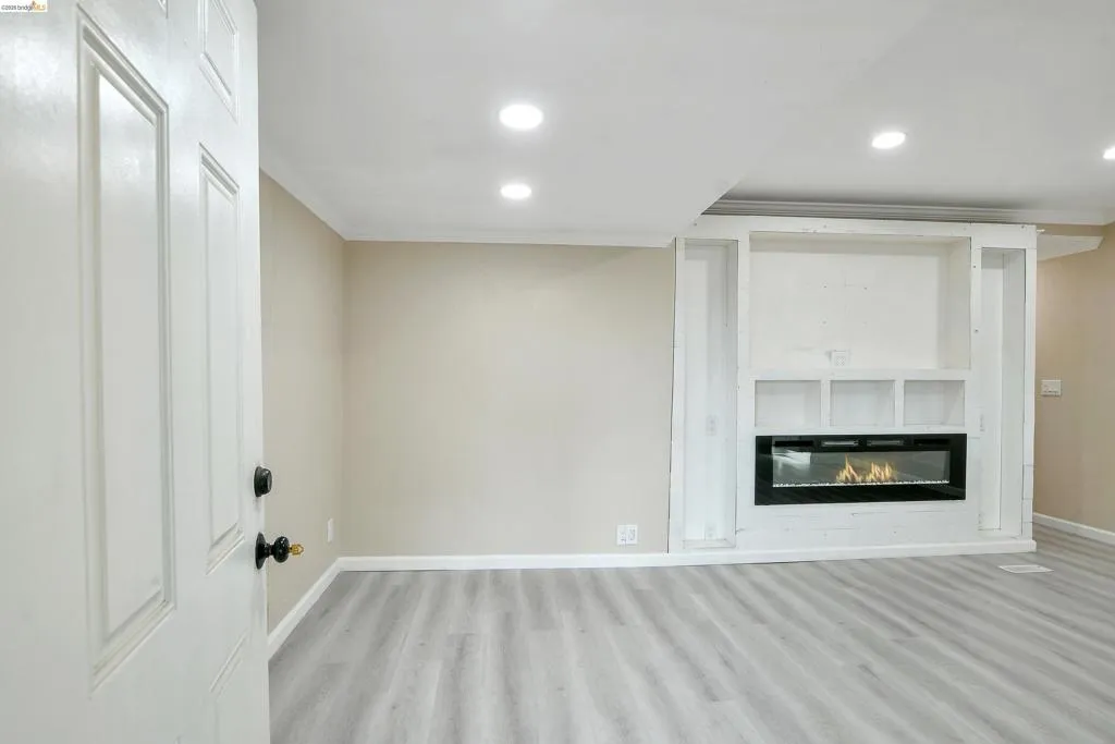 Unfurnished living room featuring light wood-type flooring, recessed lighting, a glass covered fireplace, and ornamental molding