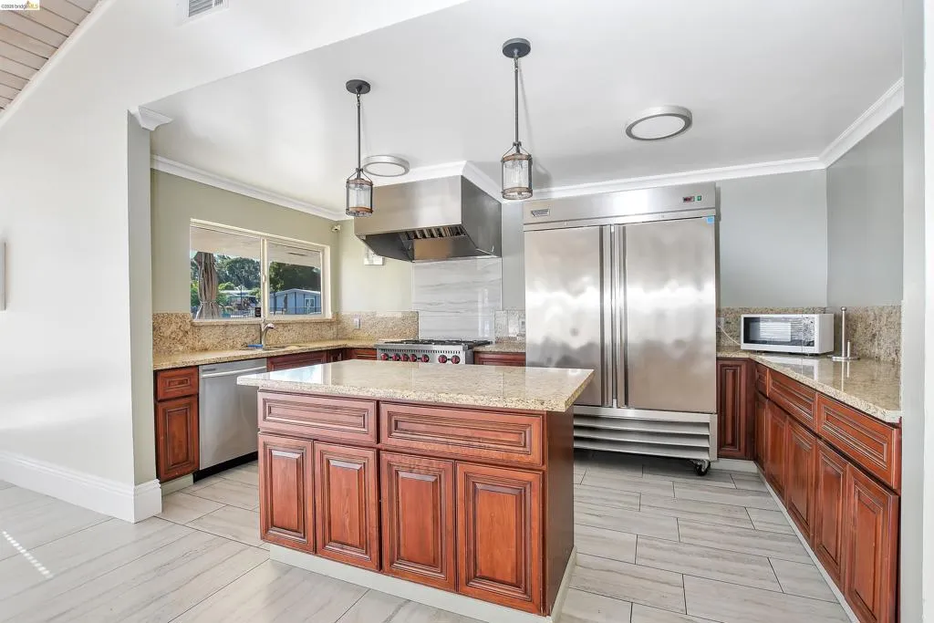 Kitchen with high end appliances, ornamental molding, a center island, light stone countertops, and backsplash