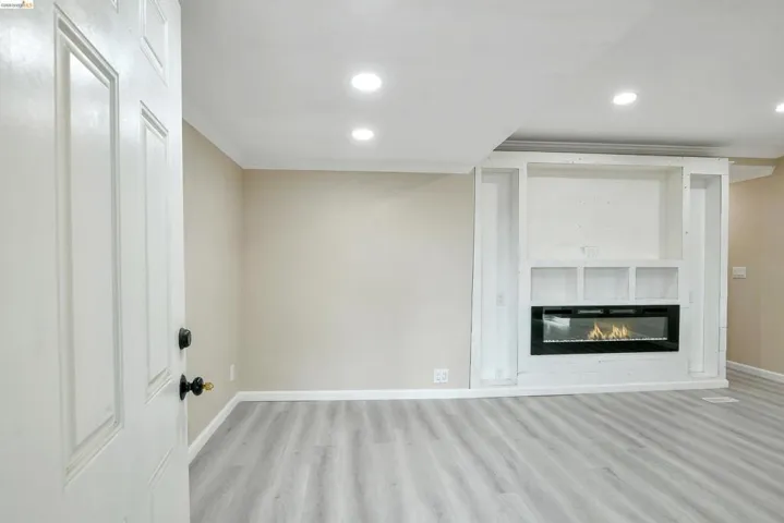 Unfurnished living room featuring light wood-type flooring, recessed lighting, a glass covered fireplace, and ornamental molding