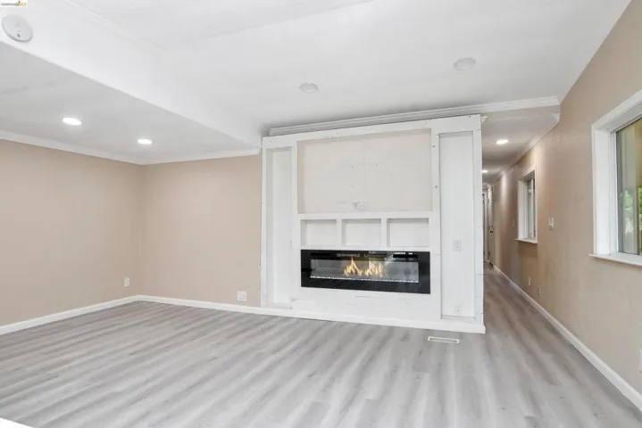 Unfurnished living room with ornamental molding, recessed lighting, light wood finished floors, and a glass covered fireplace