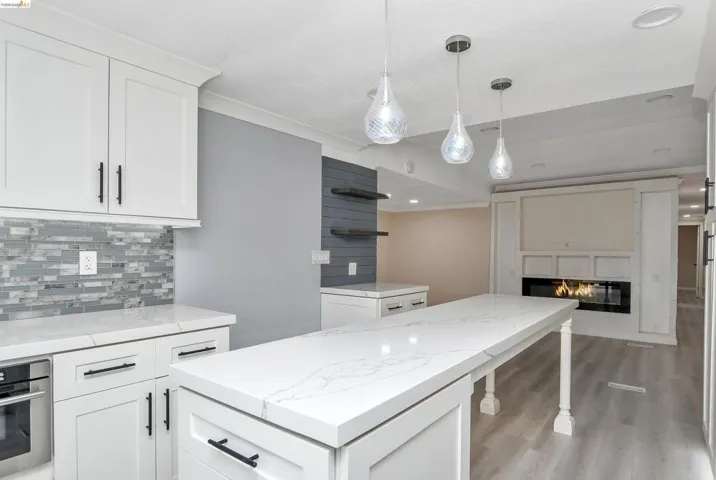 Kitchen featuring white cabinetry, decorative backsplash, a kitchen bar, pendant lighting, and a glass covered fireplace