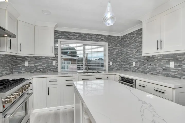 Kitchen featuring stainless steel appliances, white cabinets, light stone counters, decorative light fixtures, and ornamental molding