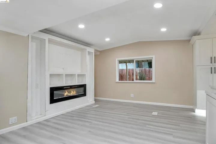 Unfurnished living room with ornamental molding, lofted ceiling, light wood-style flooring, a glass covered fireplace, and recessed lighting