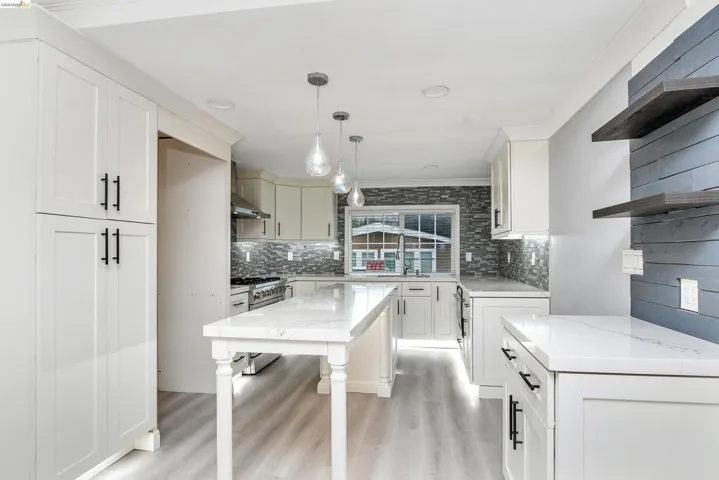Kitchen featuring open shelves, pendant lighting, light wood-style floors, light stone counters, and backsplash