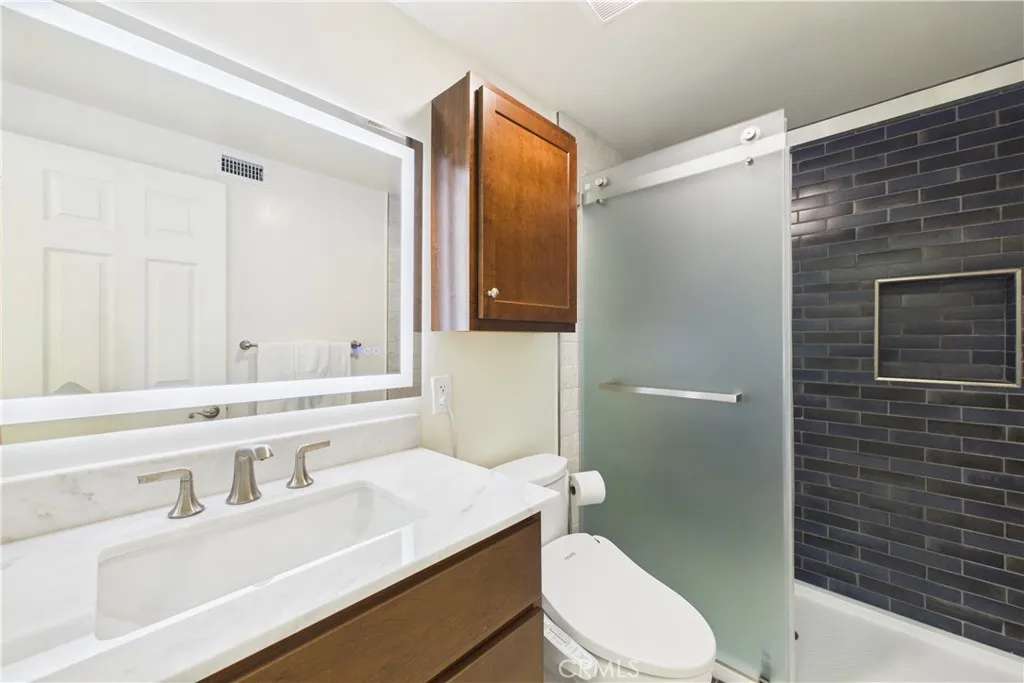 Primary bath with a lit mirror, storage, and tiled shower with dual shampoo boxes