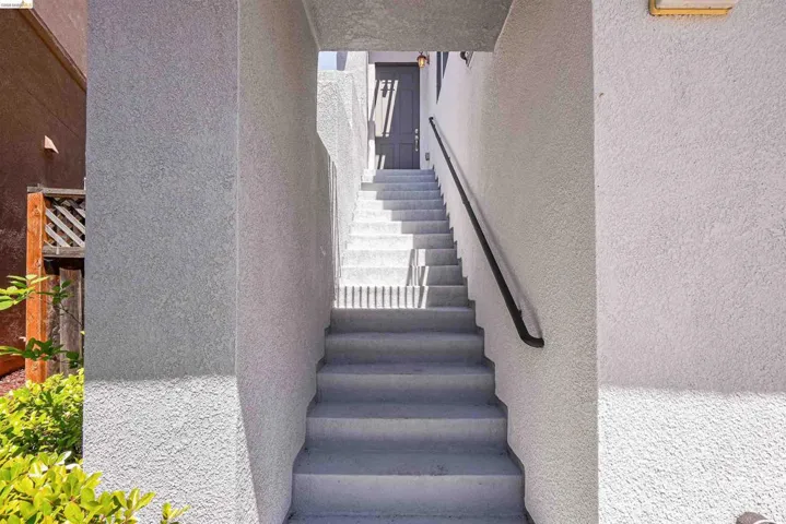Stairway entrance featuring stucco walls, a dark-toned door, and a black handrail