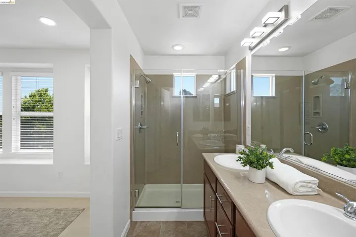 Double vanity with integrated sinks, a glass-enclosed shower, wood-finish cabinetry, and recessed lighting