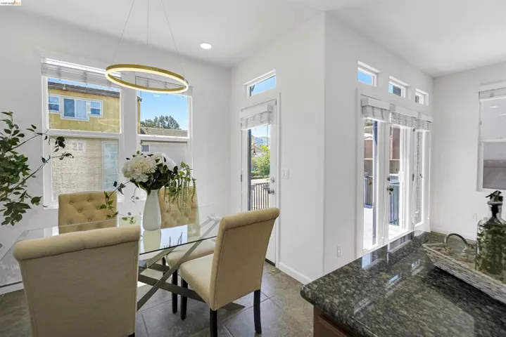 Dining area with a modern circular chandelier, multiple windows, French doors, and stone tile flooring