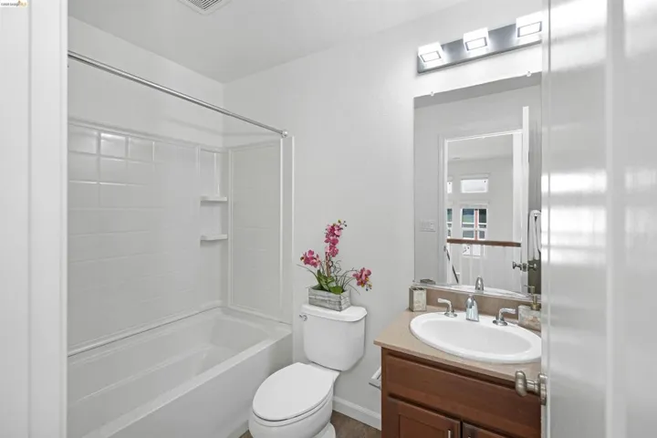 Full bathroom featuring a white tub and shower combination with integrated shelving, a single vanity with a light-colored countertop, and a wood-finish cabinet