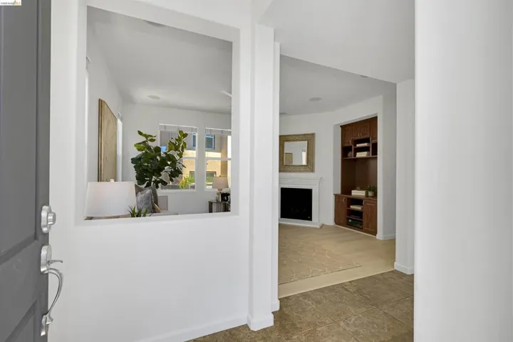 Entryway featuring large format floor tiles, a built-in media center with wood-finish cabinetry, a fireplace with a white mantel, and a decorative interior window