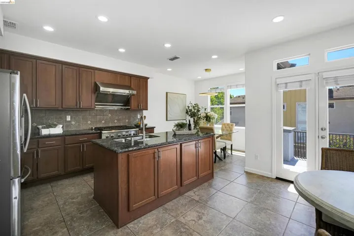 Kitchen featuring wood cabinetry, granite countertops, tile flooring, and stainless steel appliances including a gas range and refrigerator