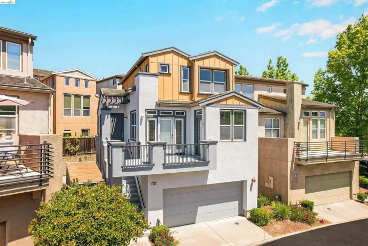 Multi-level modern residence featuring a two-car garage, multiple balconies with dark iron railings, and a distinct architectural style with varied facade materials including stucco and vertical wood siding