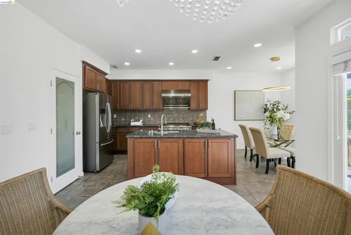 Open-concept kitchen featuring wood cabinetry, dark stone countertops, stainless steel appliances, and tile flooring