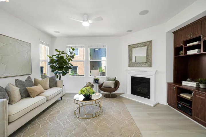 Spacious living area featuring light wood-finish flooring, multiple windows, a white ceiling fan, and a fireplace with a white mantel
