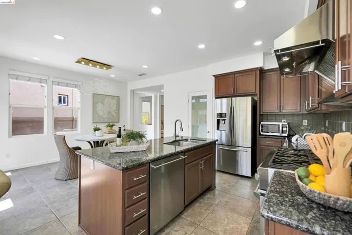 Gourmet kitchen featuring a large central island with a stainless steel sink, granite countertops, stainless steel appliances, recessed lighting, and rich wood cabinetry
