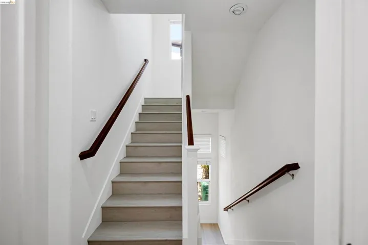 Multi-level interior featuring light wood-finish stair treads with dark wood handrails, recessed ceiling lighting, and crisp white wall finishes
