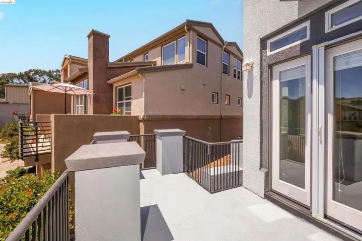 Spacious exterior balcony featuring durable light-colored surfacing, dark metal railings, and dual glass-paned doors