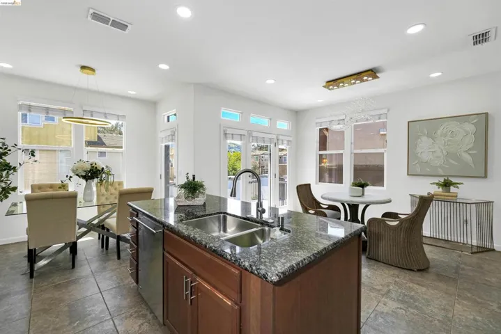 Kitchen island with wood cabinetry and a stone countertop features an undermount double-basin sink and a gooseneck faucet