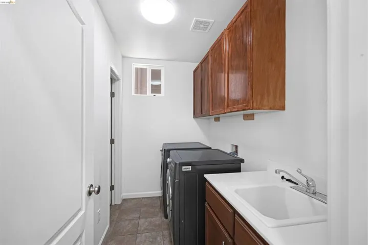 Dedicated laundry area featuring a utility sink with a chrome faucet, wood-finish cabinetry, and tiled flooring