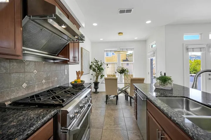 Gourmet kitchen featuring a professional-grade gas range, stainless steel range hood, stone tile backsplash, granite countertops, and rich wood cabinetry