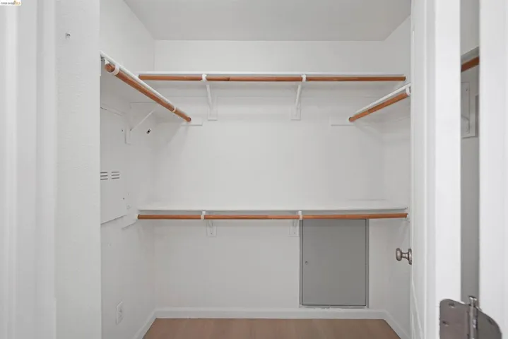Walk-in closet featuring white shelving, wood-finish hanging rods, and wood-finish flooring