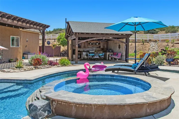 Spa with cascading waterfall, center island lounging area and covered outdoor kitchen