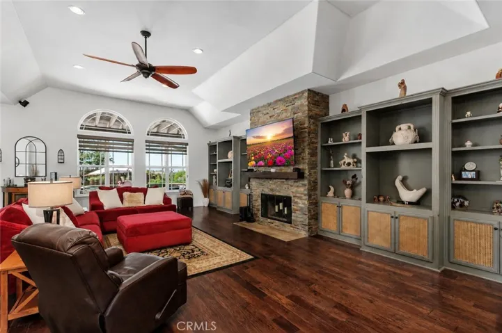 Spacious family room with coffered ceiling, hardwood flooring, ceiling fan, stacked stone floor to ceiling fireplace and custom built-ins