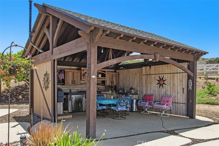 Outdoor covered kitchen with sliding barn doors, Traeger, Twin Eagle Teppan grill & refrigerator, stainless steel sink, lights custom cabinetry & dining area