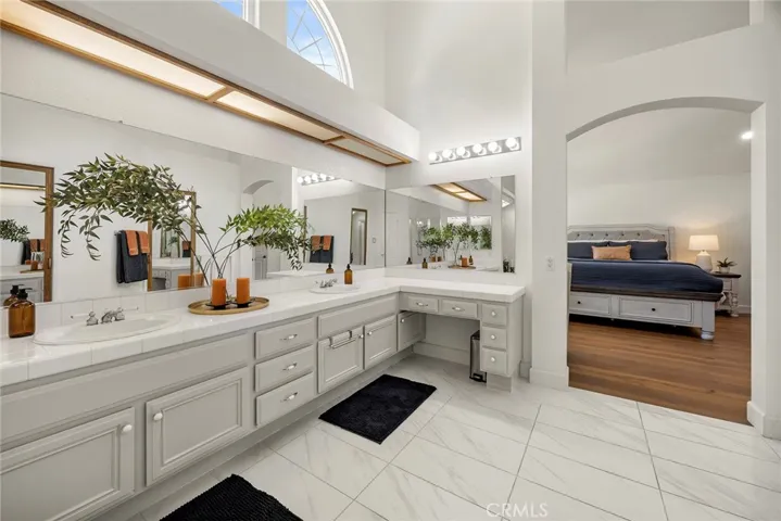 High ceilings and large windows make this en suite bath feel like a spa sanctuary. Dual sinks on the left provide lots of room for getting prepared to face the day. The make up vanity is at the far end of the counter.