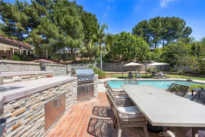 Outdoor kitchen island includes covered BBQ grill, refrigerator and bar-height countertops with storage.